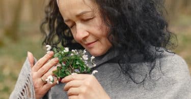 Mulher segurando flor de olhos fechados e sentindo seu aroma