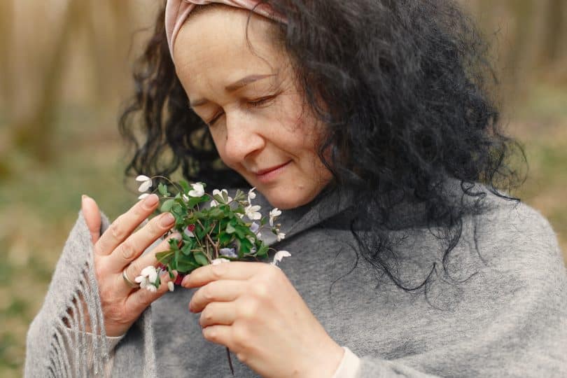 Mulher segurando flor de olhos fechados e sentindo seu aroma