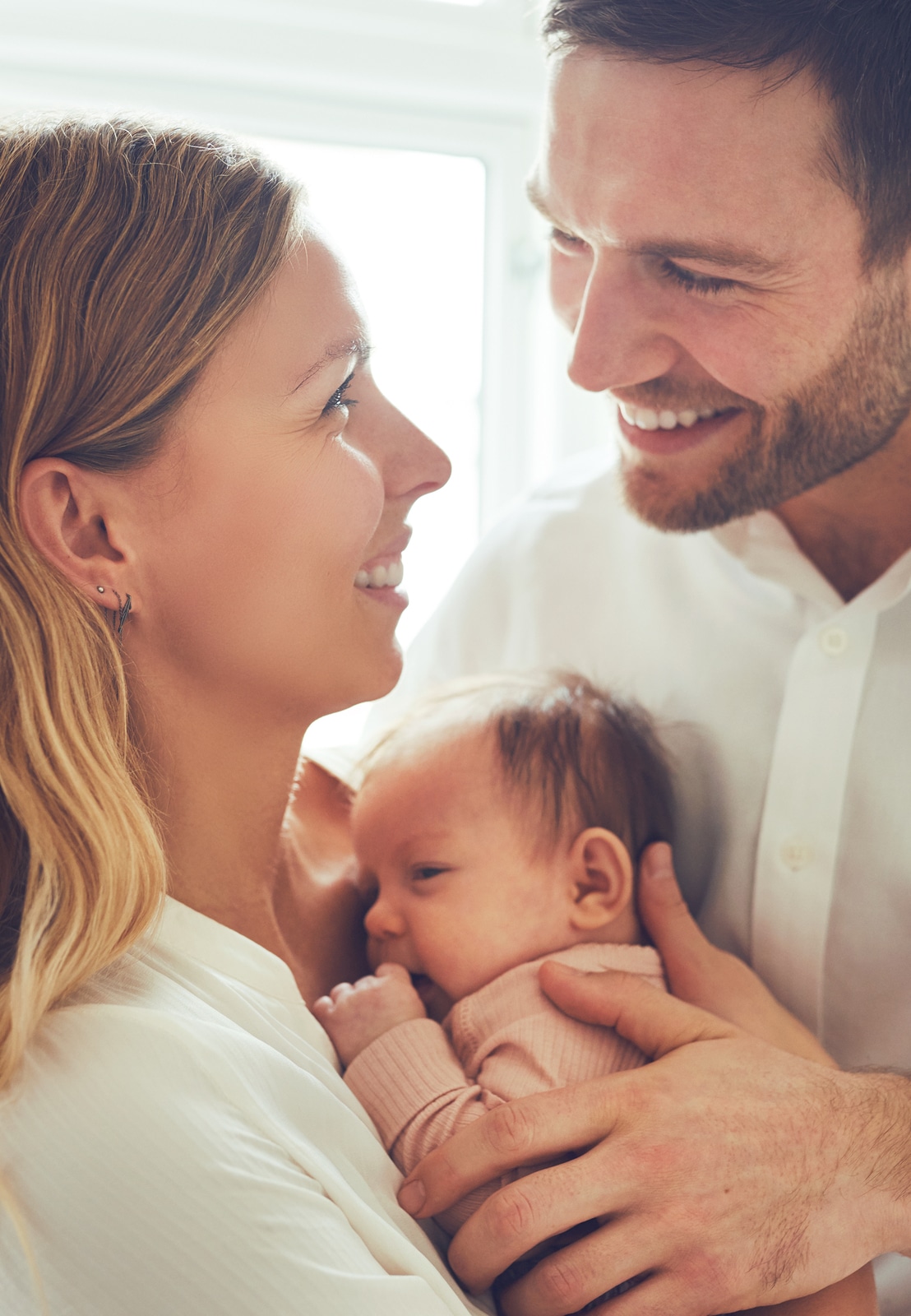 Smiling mother and father holding their newborn baby daughter at home