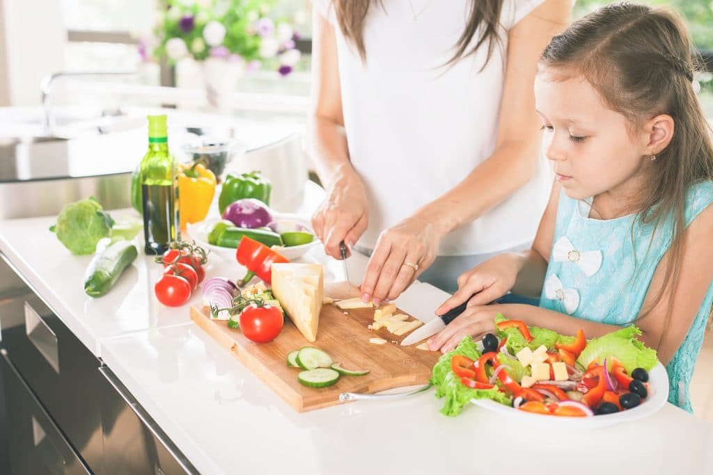 Cute little girl cooking with her mother. Healthy food, cooking healthy salad with vegetables ingredients. Mom and daughter cooking together. Recipe food for baby or child