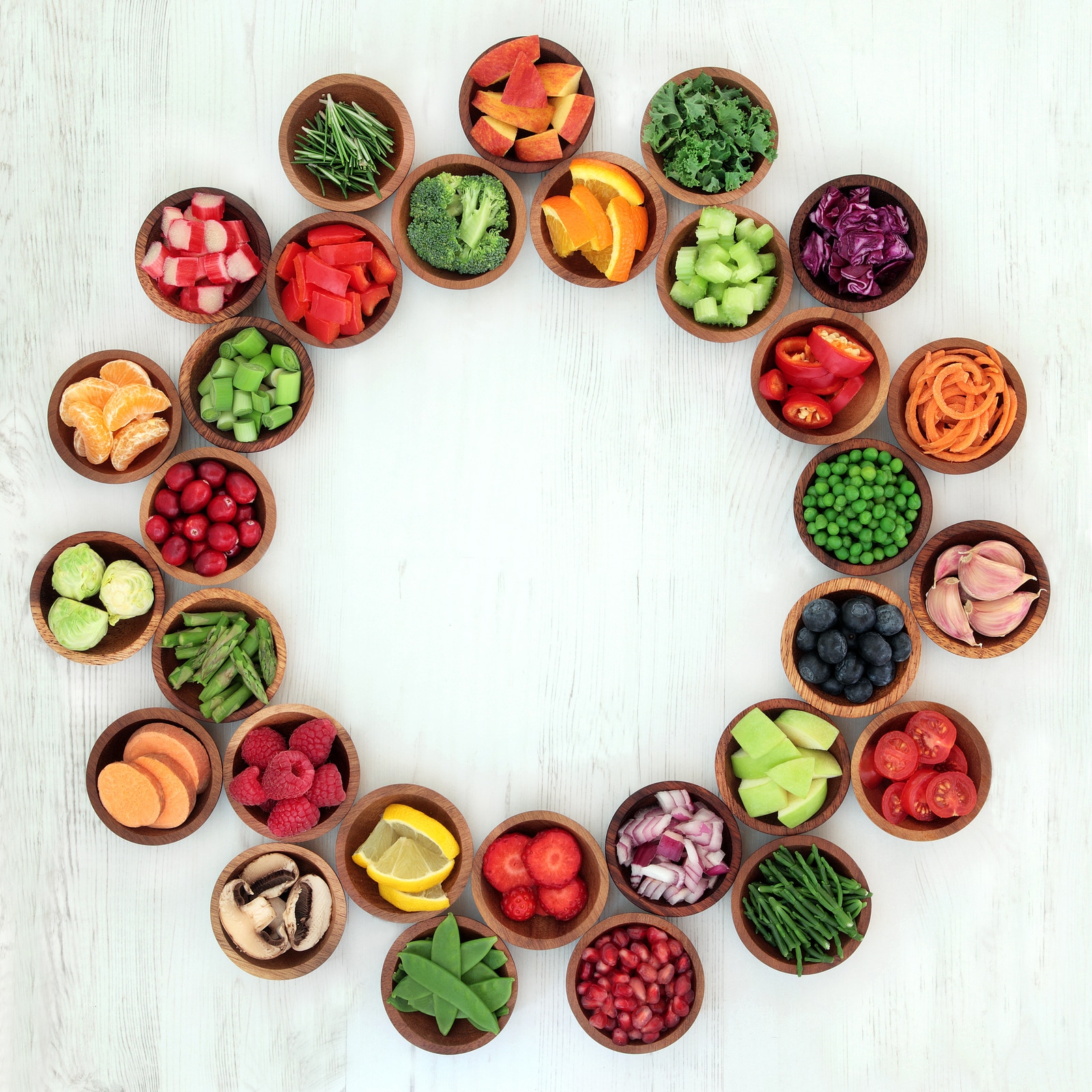 Paleo diet health and super food of fruit and vegetables in wooden bowls forming an abstract wheel over distressed white wood background. High in vitamins, antioxidants, minerals and anthocyanins.