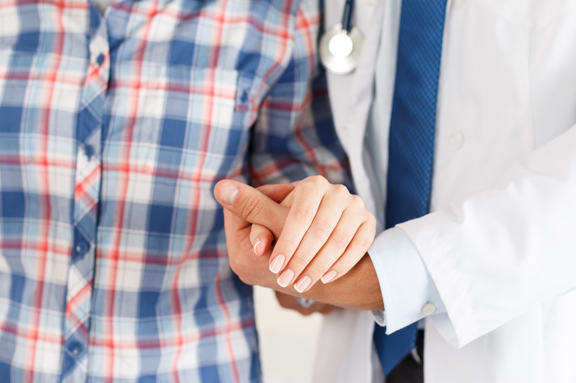 Friendly male doctor's hands holding female patient's hand for encouragement and empathy. Partnership trust and medical ethics concept. Bad news lessening and support. Patient cheering and support