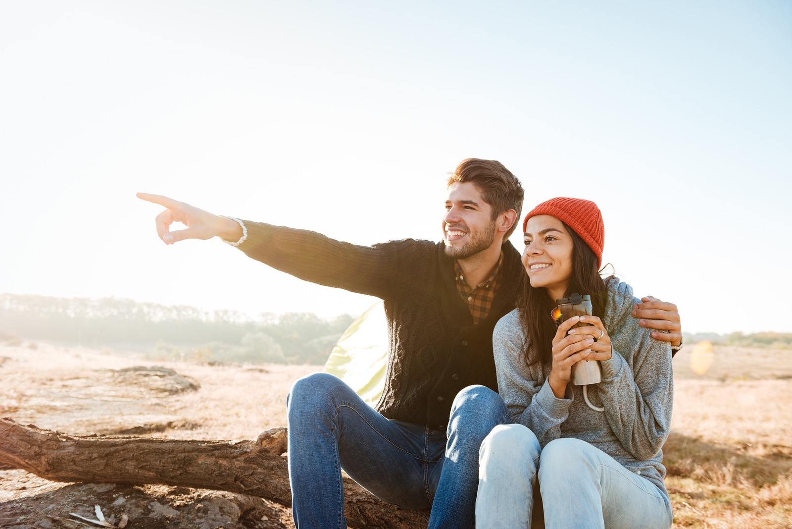 Smiling couple near the tent. man shows away. couple sitting on log