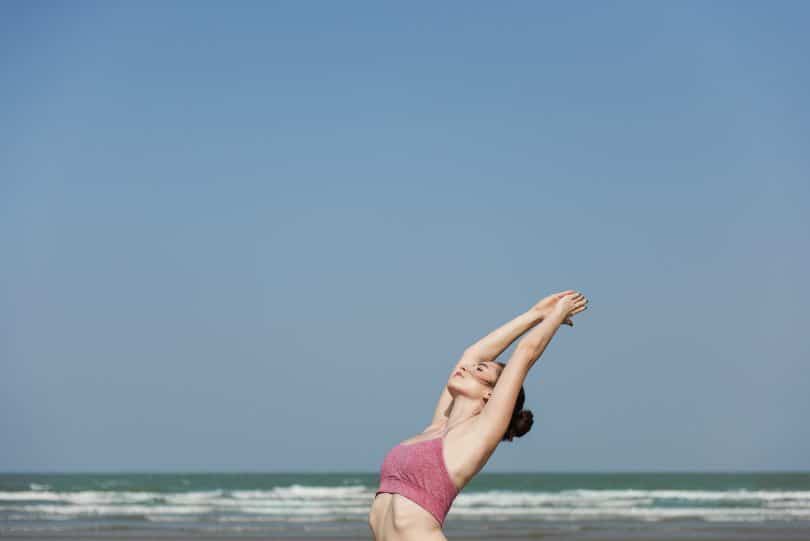 Mulher na praia de top com braços unido no alto meditando