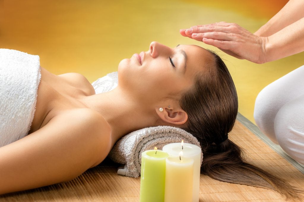 Close up portrait of attractive young woman having alternative treatment therapy. Therapist's hands on woman's forehead.