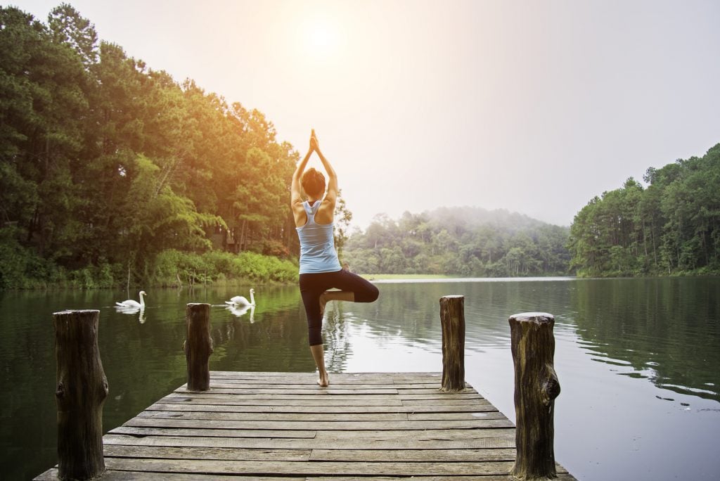 Young healthy woman practicing yoga on the bridge in the nature