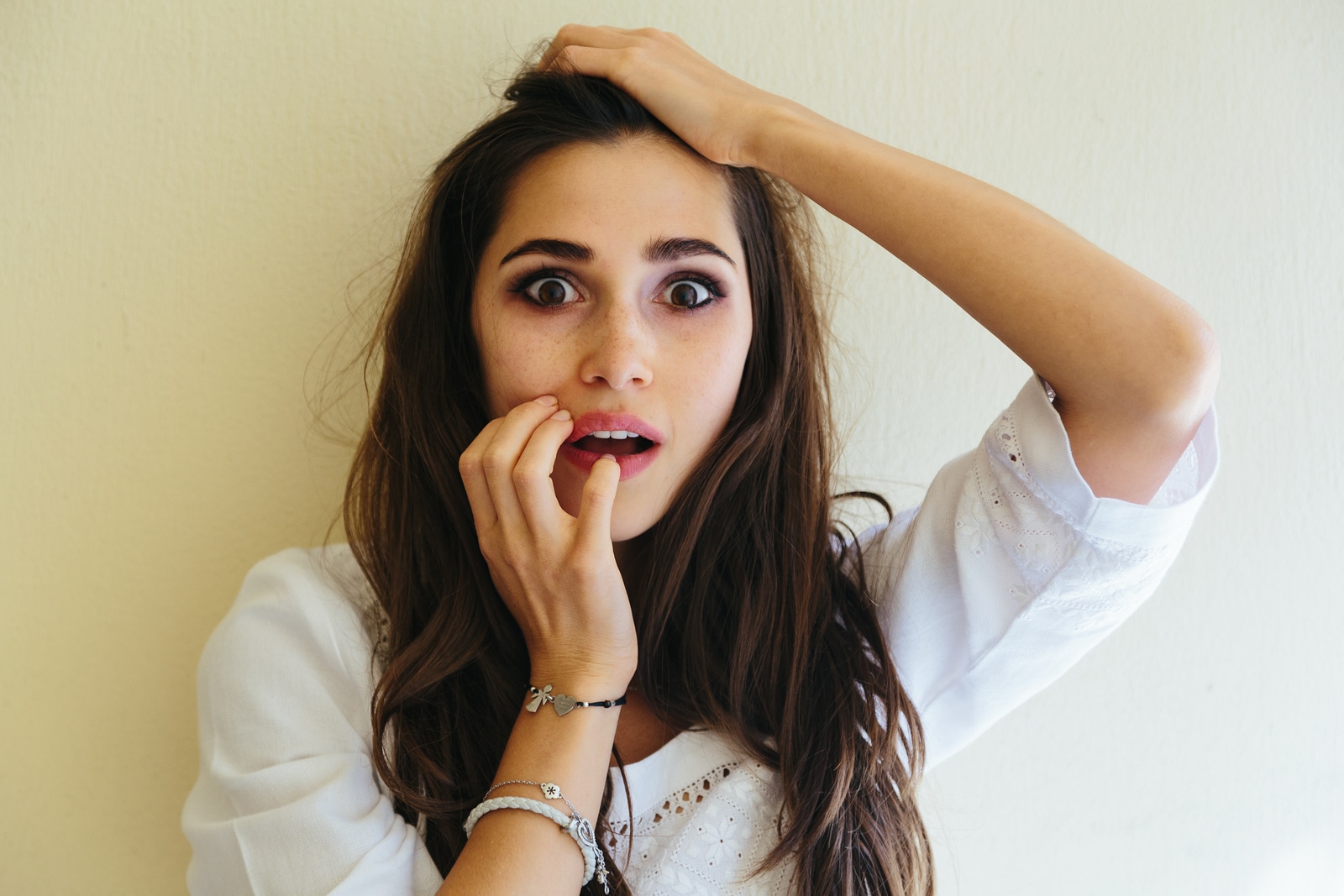 Close-up portrait of young woman scared, afraid and anxious biting her finger nails, looking straight into camera with wide opened eyes isolated on yellow background. Human emotions concept. Copy space text.