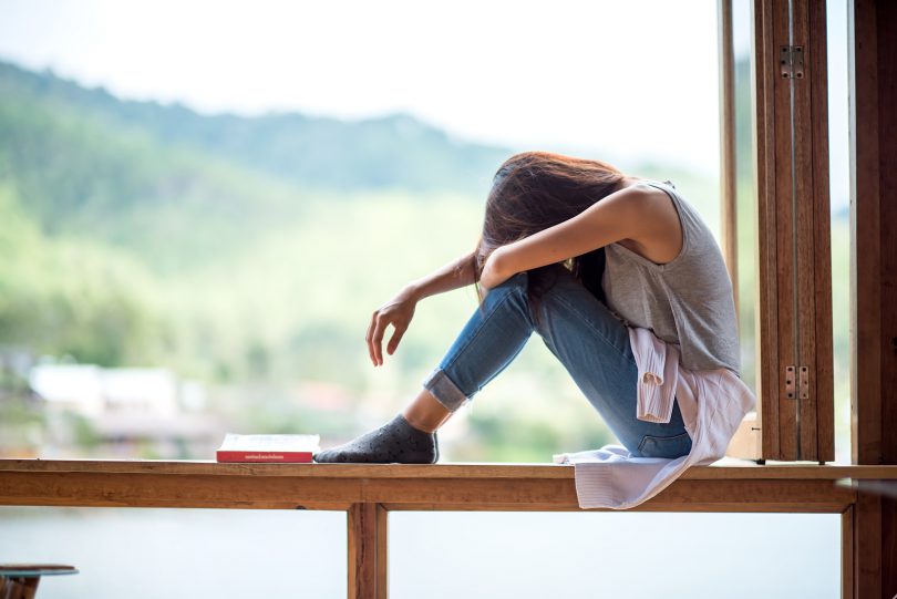 Jovem mulher atraente sentada em uma janela com humor solitário