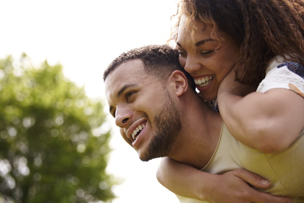 Close up of young adult couple piggybacking outdoors, side view