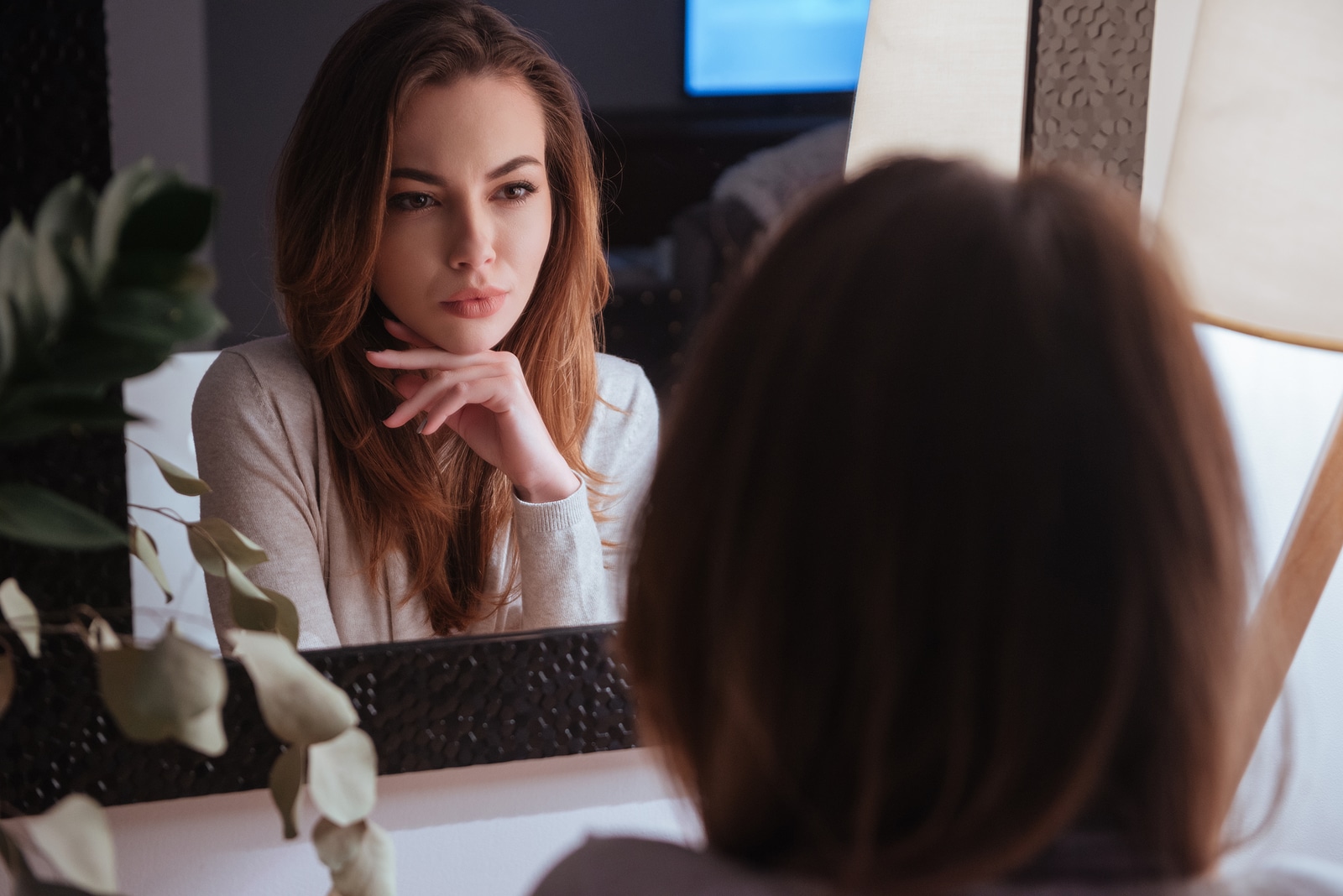 Young beautiful woman smiling to herself in mirror while sitting at bedroom