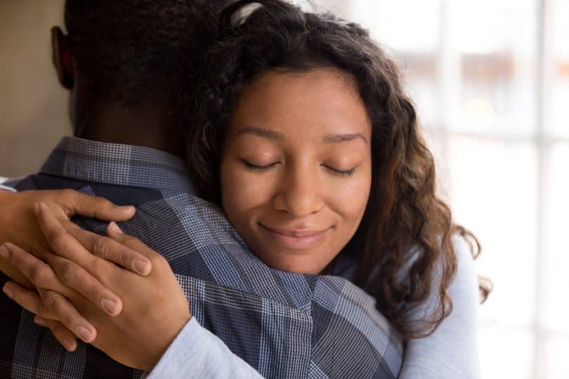 Mulher negra abraçando homem negro com expressão relaxada