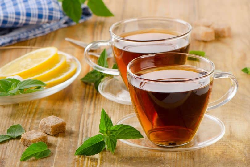 Xícaras de chá de vidro com hortelã e limão em uma mesa de madeira.