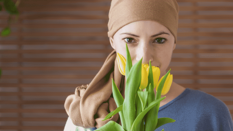 Mulher com um pano enrolado n a cabeça segurando um buquê de tulipas amarelas