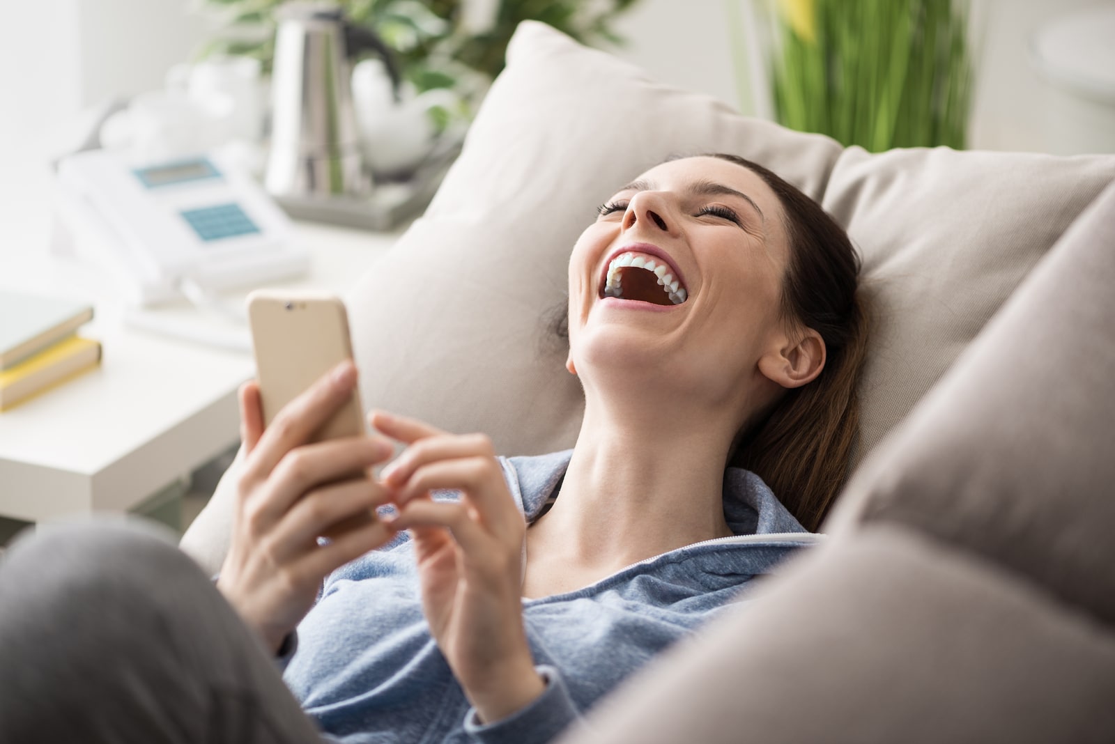 Relaxed smiling woman on the couch at home she is using a smartphone and laughing