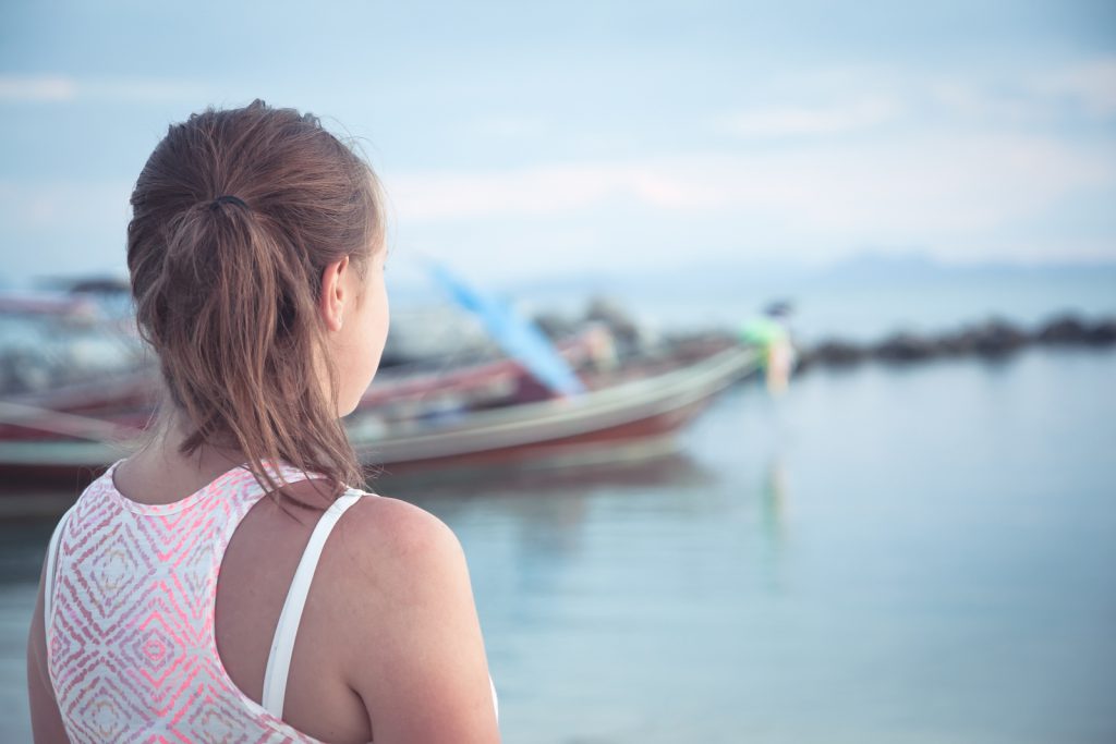 Teenager girl looking into the distance on tropical beach at sunset during summer holidays. Sunlight illuminate girl face