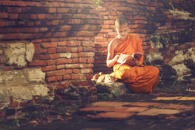 Menino budista sentado lendo um livro.