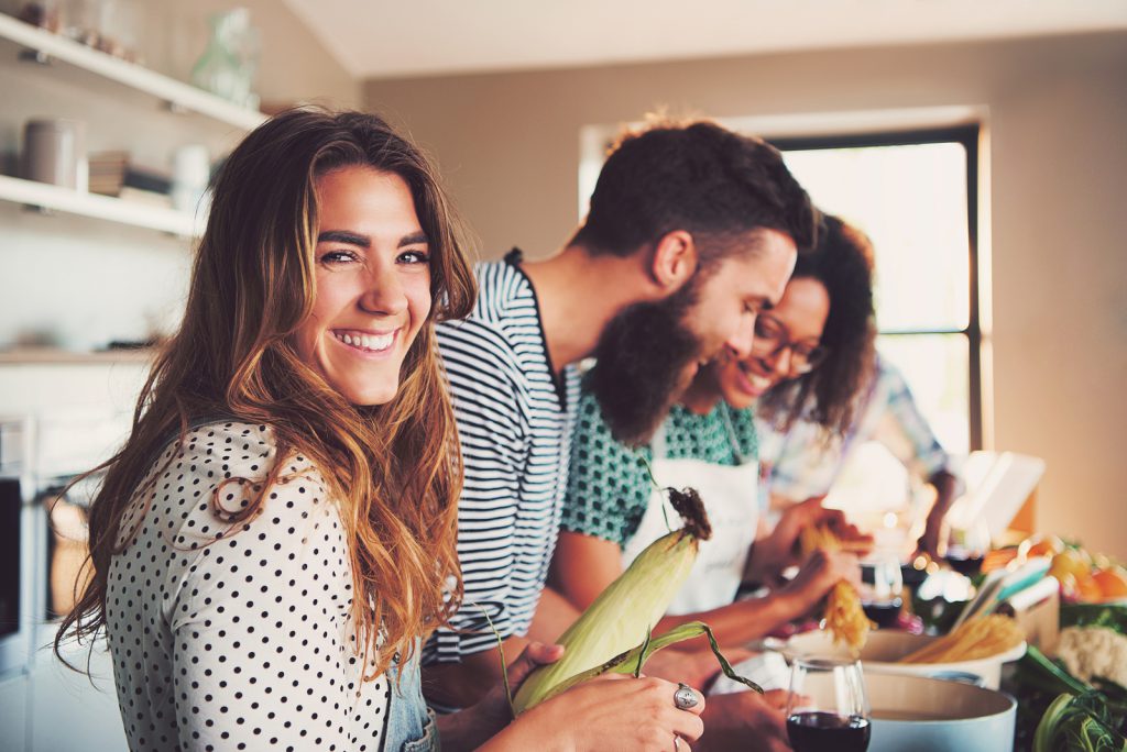 Laughing woman talking and preparing meals at table full of vegetables and pasta ready for cooking in kitchen