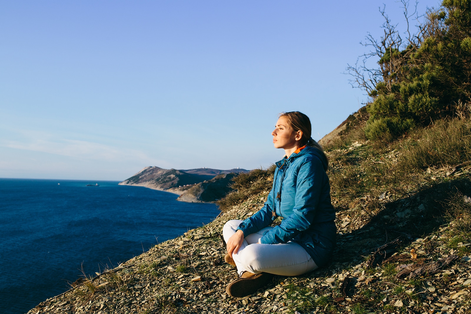 young woman traveler sitting on top of a cliff and looking at sea. Travel Holidays Freedom and Lifestyle Concept