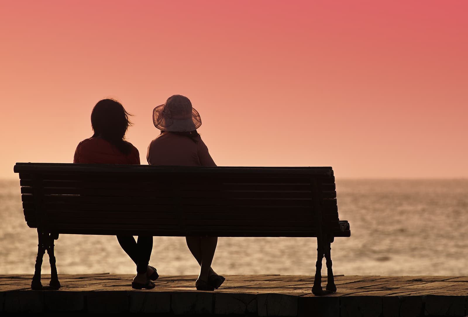 Silhouette of two women on a bench by the sea