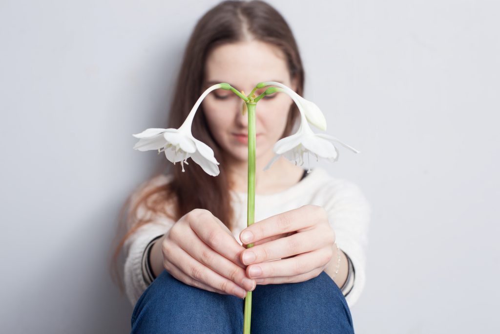 girl holding a flower and looking down sadly.