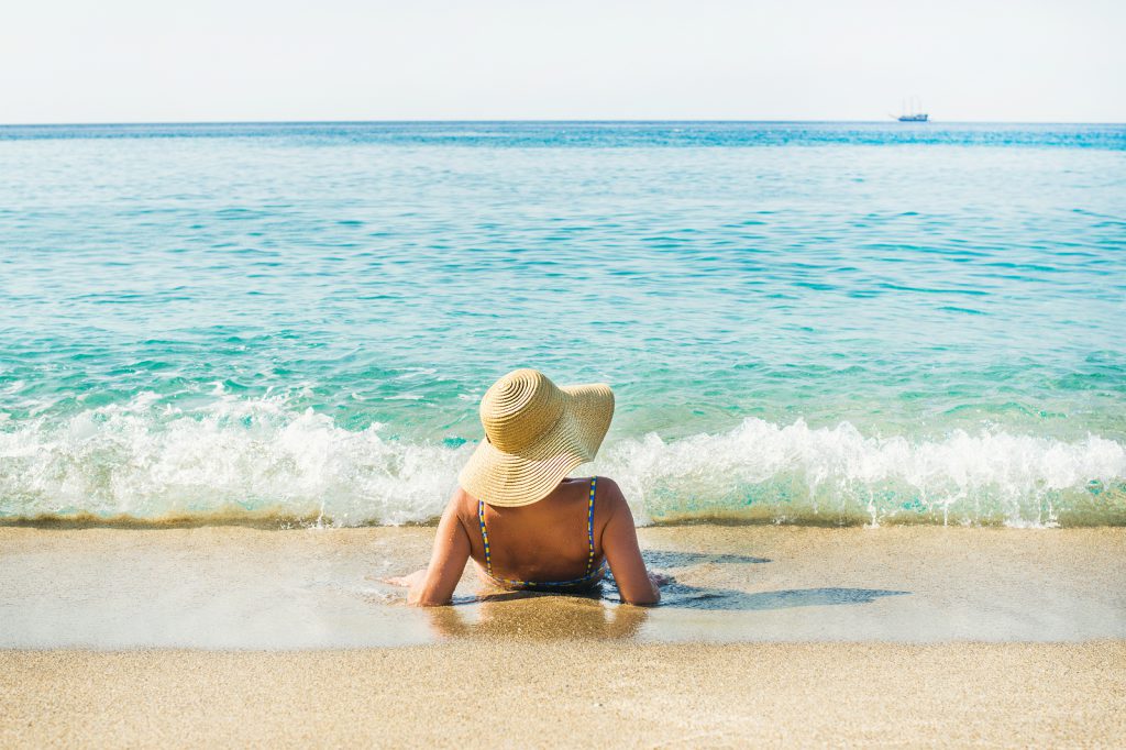 Tanned tourist woman in swimsuit and hat lying on sand and enjoying clear blue waters of Mediterranean sea at Cleopatra beach, Alanya, Mediterranean region, Turkey