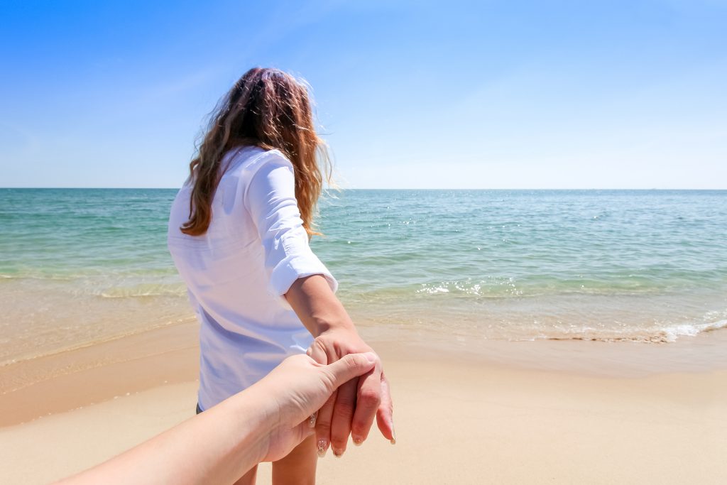 Back view of a couple taking a walk holding hands on the beach