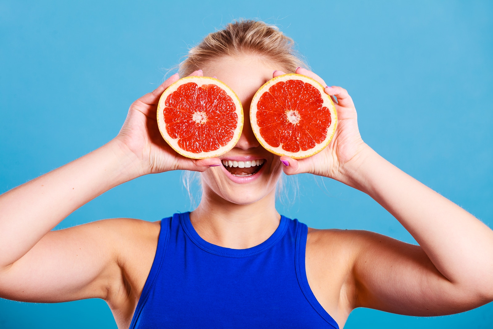 Woman fit girl holding two halfs of grapefruit citrus fruit in hands covering her eyes. Healthy diet food. Happiness holidays fun concept.