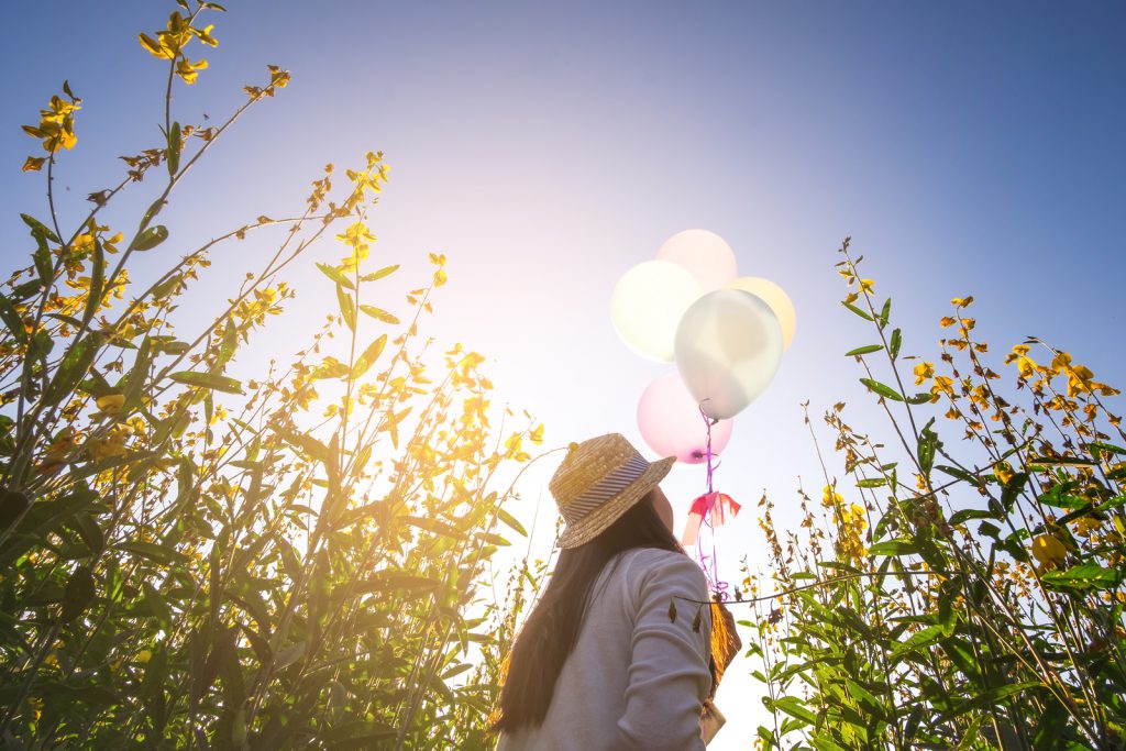 Girl running on the field of yellow flowerwith balloons at sunset. Happy woman on nature concept about carefree airiness and relax vintage effect.