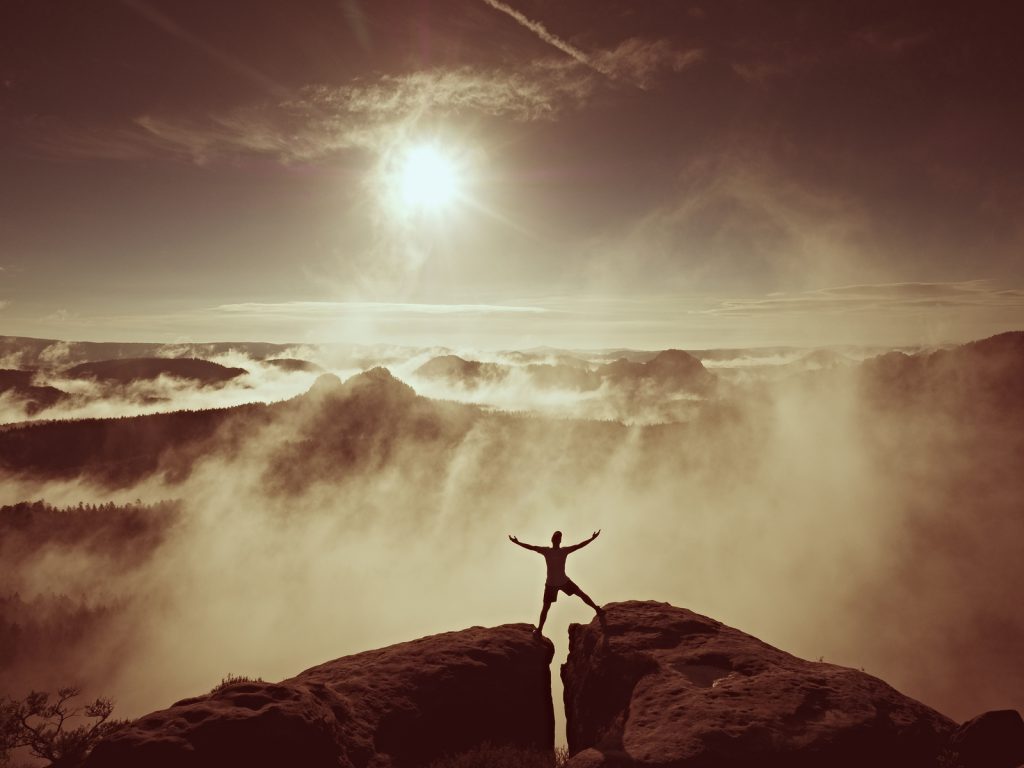 Happy man gesture of triumph with rams in air. Funny hiker on peak of sandstone rock in national park Saxony Switzerland watching to horizon