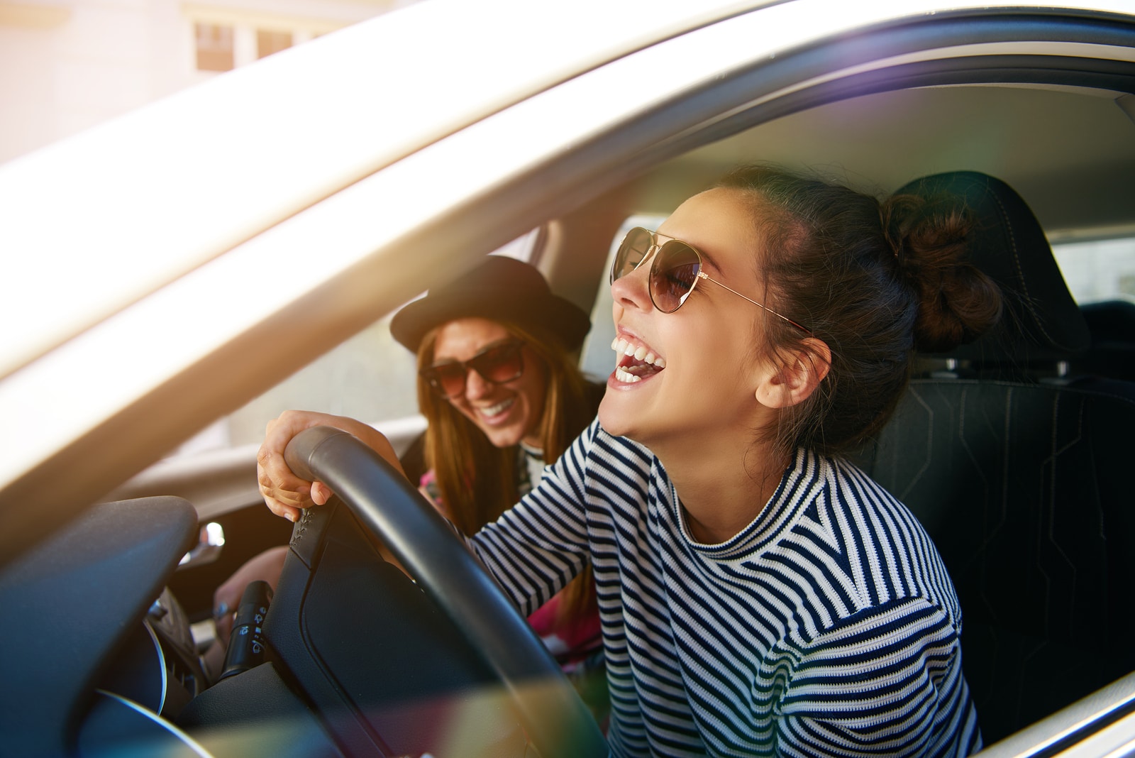 Laughing young woman wearing sunglasses driving a car with her girl friend close up profile view through the open window