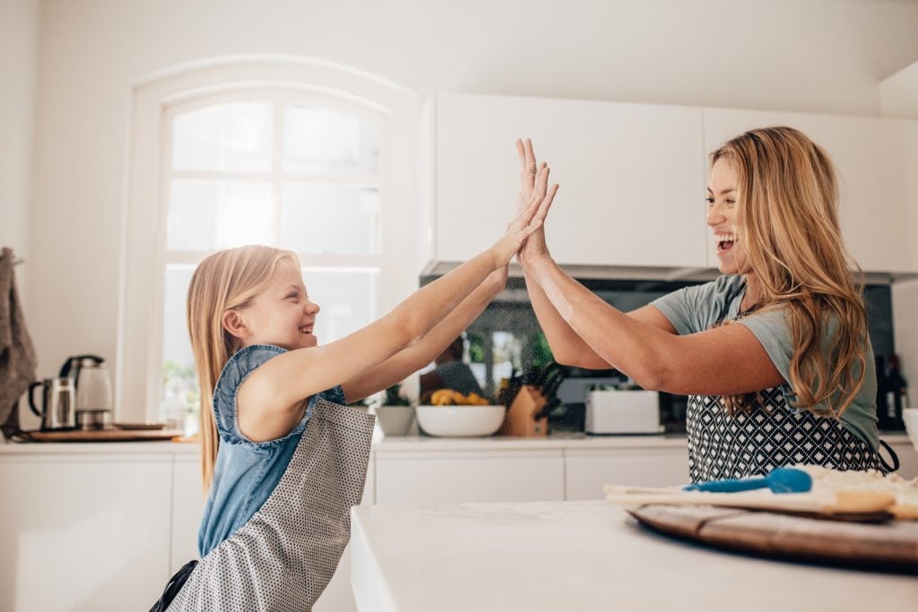 Little girl and her mother in kitchen giving high five. Mother and daughter in kitchen cooking.