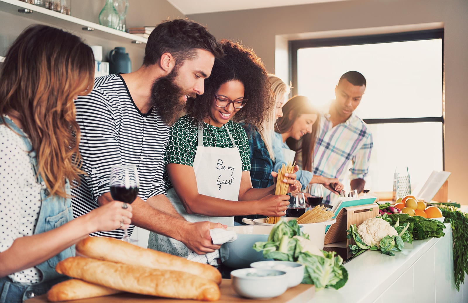 Multiracial funny friends cook some tasteful food at kitchen while drinking wine.