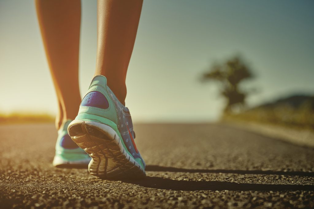 Closeup of female runner shaved feet in running shoes going for a run on the road at sunrise or sunset. Shallow depth of field toned with instagram like filter flare effect.