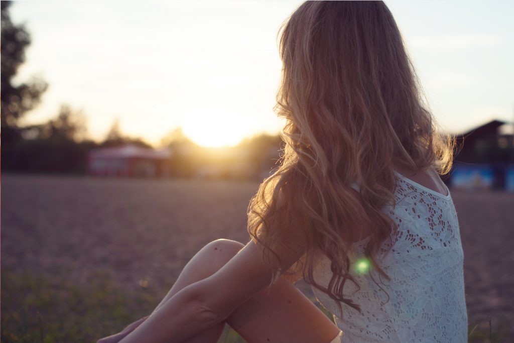 Sunny portrait of a beautiful young romantic woman or girl in white dress on beach watching the sunset enjoying nature summer evening outdoors. Soft light. Sunshine. Toned warm colors