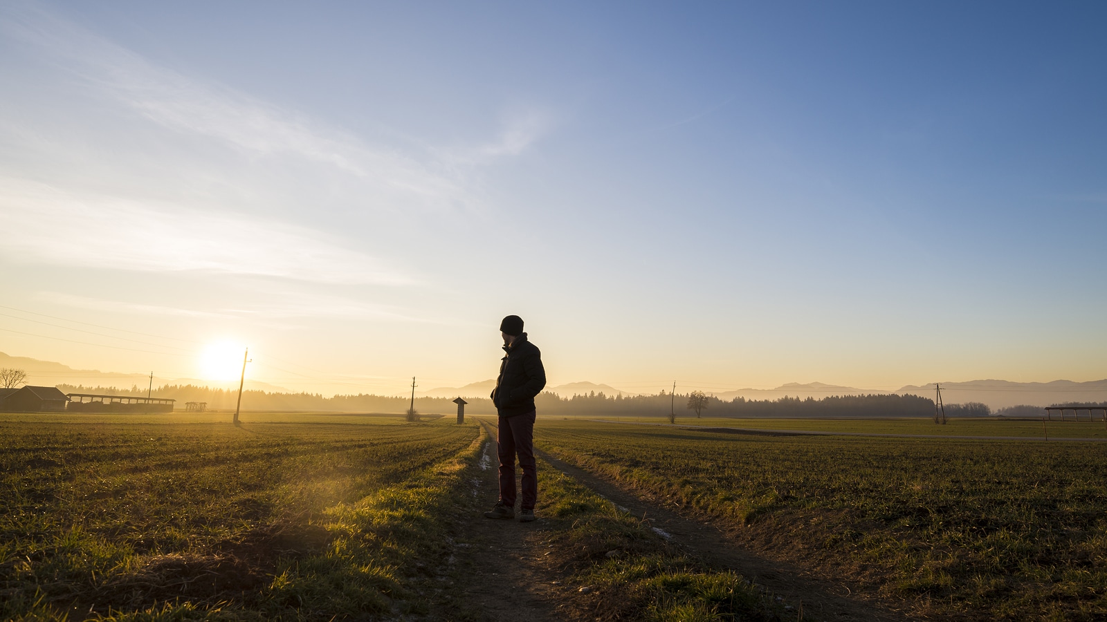 Young man standing on country road in a beautiful landscape looking back towards a setting evening sun.