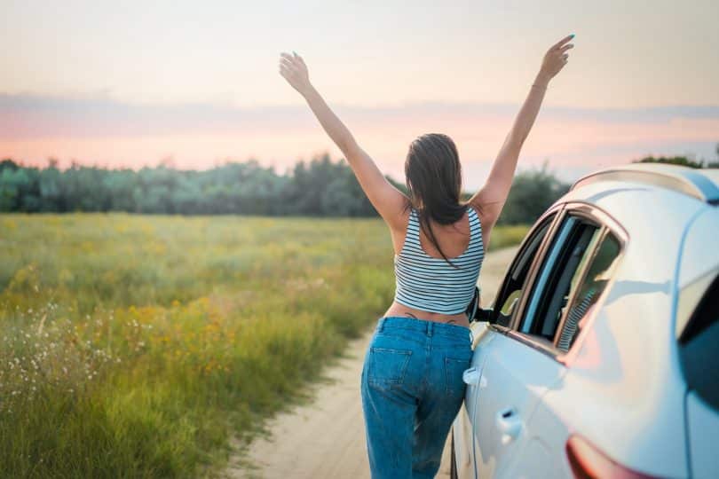 Mulher encostado no carro com os braços para cima