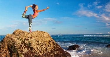 Mulher faz yoga sobre rocha.