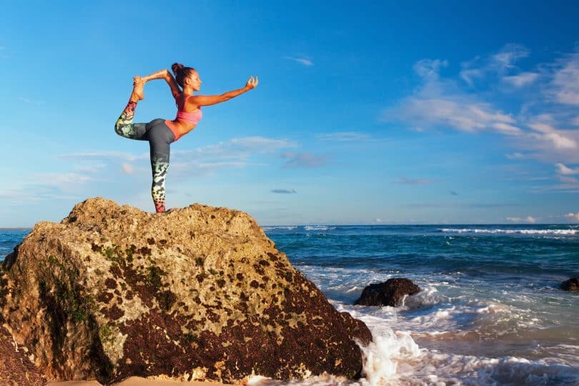 Mulher faz yoga sobre rocha.