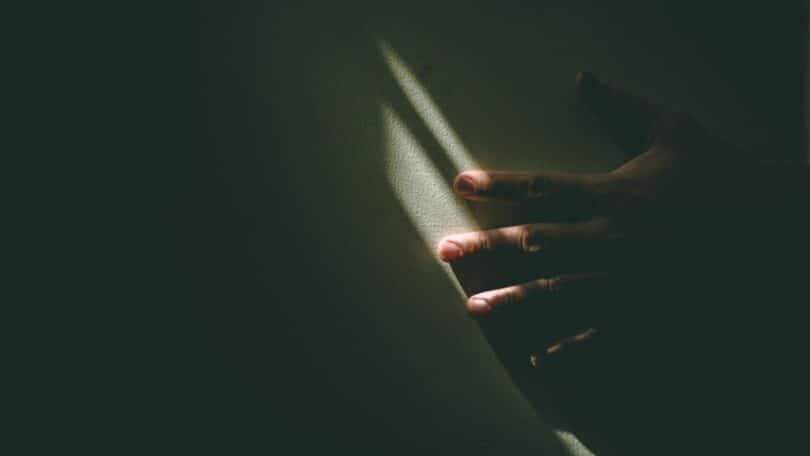 Imagem da mão de uma pessoa na parede e apenas um feixe de luz, iluminando