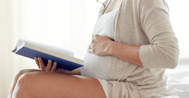 Mulher grávida sentada lendo um livro com a mão sobre a barriga.