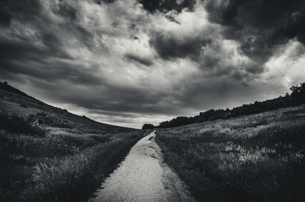 Paisagem em preto e branco de uma estrada que leva a um campo gramado antes de uma tempestade.