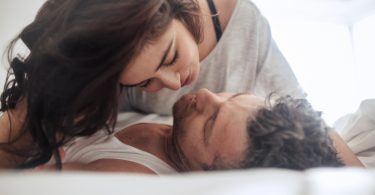 Young couple caressing lying in bed together. Couple in a relationship kissing and cuddling.