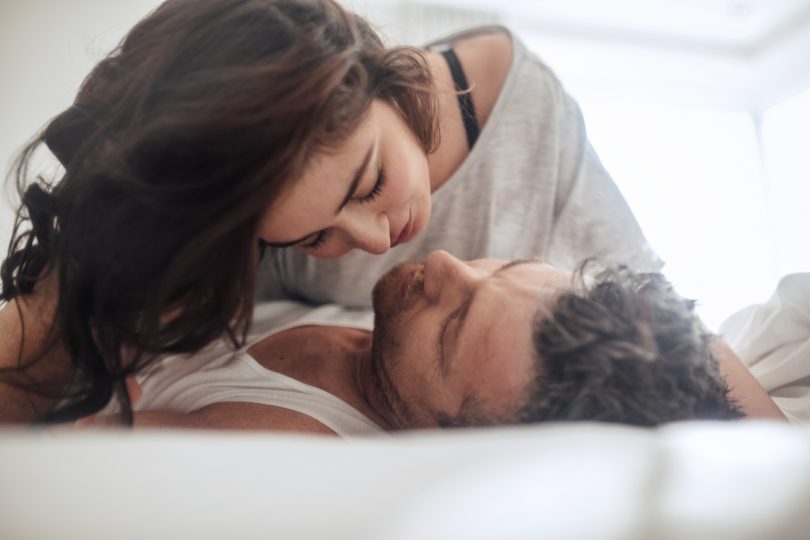 Young couple caressing lying in bed together. Couple in a relationship kissing and cuddling.