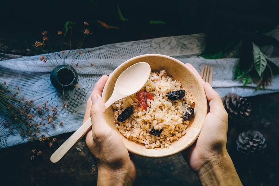 Mãos segurando tigela com arroz integral e carnes secas, e uma colher.