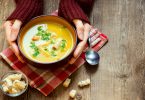 Mãos brancas femininas segurando tigela de sopa.