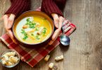 Mãos brancas femininas segurando tigela de sopa.