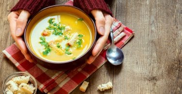 Mãos brancas femininas segurando tigela de sopa.