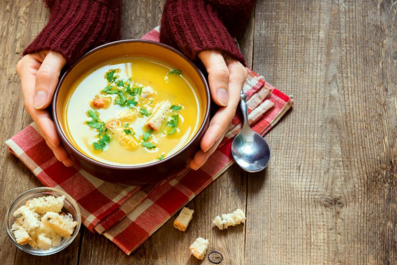 Mãos brancas femininas segurando tigela de sopa.