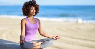 Mulher negra fazendo meditação à beira da praia