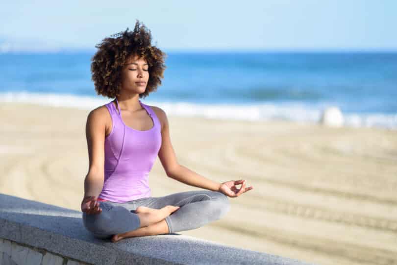 Mulher negra fazendo meditação à beira da praia